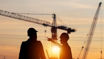 Silhouette of Engineer and foreman worker checking project at building site, construction site blurred sunset in evening time background