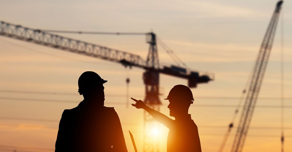 Silhouette of Engineer and foreman worker checking project at building site, construction site blurred sunset in evening time background